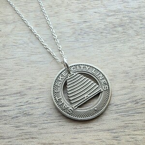 Può includere: Collana con pendente argentato. Il pendente circolare presenta le parole "SALT LAKE CITY MINES" attorno al bordo e un disegno a forma di alveare al centro. La catena della collana è argentata e delicata. Il pendente misura circa 2,5 cm di diametro.