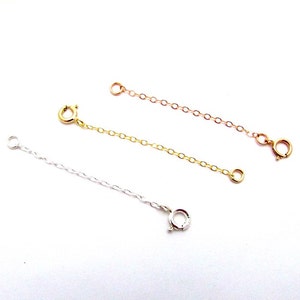 May include: Three gold chain extenders, one in silver, one in gold, and one in rose gold. Each extender has a lobster clasp on one end and a jump ring on the other.