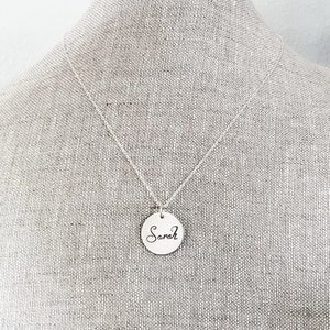 May include: A silver necklace with a round pendant that says "Sarah" in cursive.