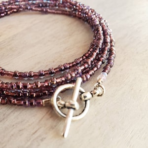 May include: A multi-strand beaded necklace with a silver toggle clasp. The beads are small and iridescent, with a purple and pink color scheme.