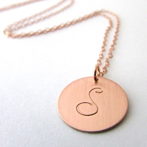 Puede incluir: Un collar de oro rosa con un colgante redondo con la letra 'S' grabada.