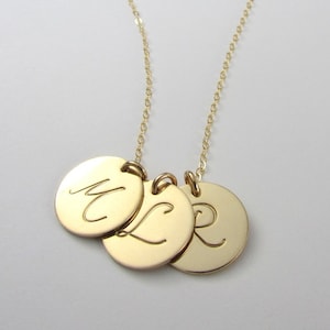 May include: A gold-colored necklace featuring three circular pendants, each engraved with a single cursive initial. The pendants are suspended from a delicate chain, creating a personalized and elegant accessory.