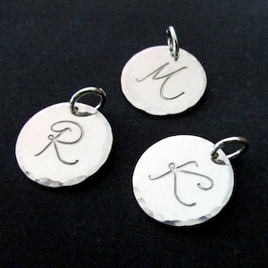 May include: Three silver charms with a hammered finish, each featuring a different letter in a cursive script. The letters are M, R, and T.