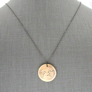 May include: A wooden pendant necklace with a circular pendant featuring a constellation design. The pendant is made of light brown wood and has a dark brown chain.