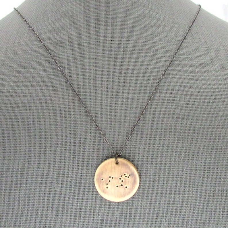 May include: A wooden pendant necklace with a circular pendant featuring a constellation design. The pendant is made of light brown wood and has a dark brown chain.