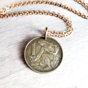 May include: A gold chain necklace with a vintage 1 lira coin pendant featuring a woman planting a tree. The coin is from Italy and has the year 1957 on it.