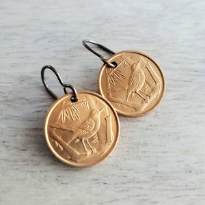 May include: Gold coin earrings with a bird design. The earrings are made from a gold-colored metal and have a simple hook closure.