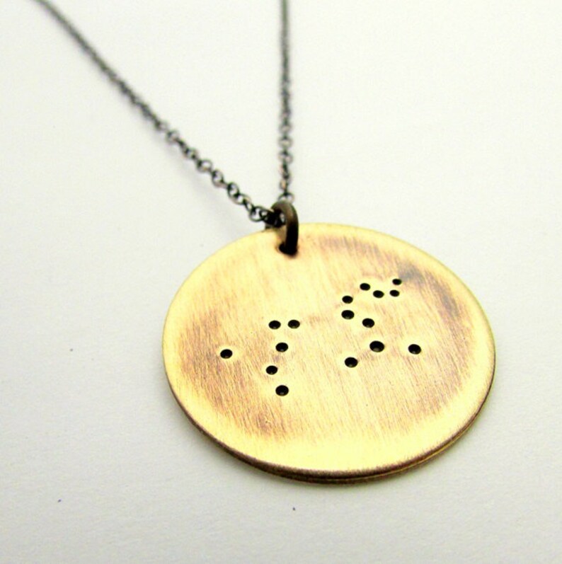 May include: A gold-toned necklace with a round pendant featuring a constellation design. The pendant has a brushed finish and is made of metal.
