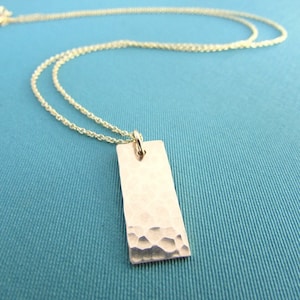 May include: A gold chain necklace with a hammered rectangular pendant.