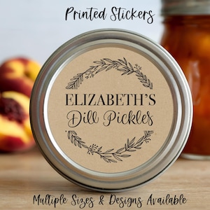 May include: A round jar lid sticker with the text "ELIZABETH'S Dill Pickles" in black script, surrounded by a botanical wreath. The sticker is on a jar with a silver lid. The words "Printed Stickers" and "Multiple Sizes & Designs Available" are also visible.