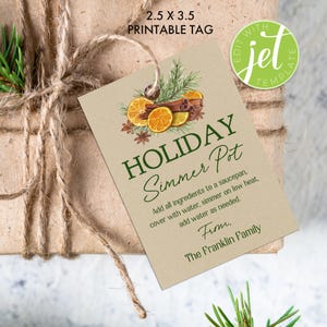 Op de afbeelding: Een rechthoekig cadeaulabel met de tekst "HOLIDAY Simmer Pot" en instructies. Het label bevat illustraties van sinaasappelschijfjes, kaneelstokjes en groen. Het label is 6,35 x 8,89 cm groot en is vastgebonden aan een ingepakt cadeau.