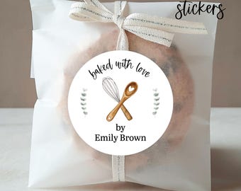 May include: A white cellophane bag tied with a ribbon, containing a baked good. A round sticker on the bag reads "baked with love" and features a whisk and spoon illustration. The sticker also includes the text "by Emily Brown" and "PRINTED stickers".