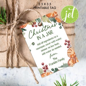 Op de afbeelding: Een rechthoekig, bedrukbaar cadeaulabel met de tekst "Christmas in a Jar" in groen script. Het label heeft aquarel illustraties van bessen en sinaasappels. Het label is met touw aan een verpakt cadeau bevestigd.