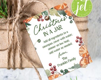 May include: A rectangular printable gift tag with the text "Christmas in a Jar" in green script. The tag features watercolour illustrations of berries and oranges. The tag is tied to a wrapped gift with twine.