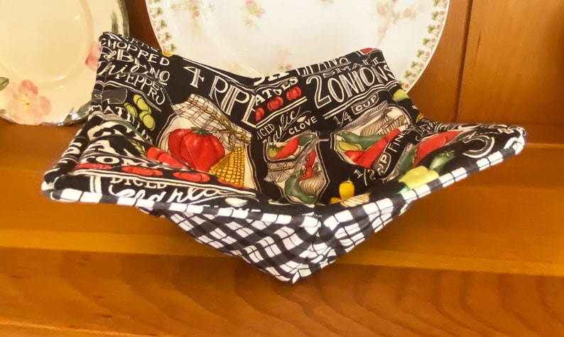 May include: Black and white fabric bowl with a checkered pattern on the bottom. The bowl is lined with a black fabric with a white print of various vegetables and spices, including onions, peppers, garlic, and tomatoes. The text on the fabric reads "4 RIP ATES 2 ONIONS 1/4 CUP 1/2 CUP FINED DICED CHOPPED PEPPRO".