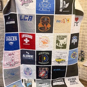 May include: A memory quilt constructed from various t-shirt panels featuring diverse graphic prints, including logos for Fender, Lifeguard, The Beatles, and Hard Rock Cafe, alongside text such as Battle Blue, Altruismo, and 8th Grade 2020 Quarantined.
