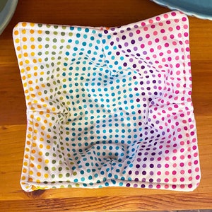 May include: A colorful bowl cozy with a white background and a rainbow polka dot pattern. The cozy is made of fabric and has a quilted design.