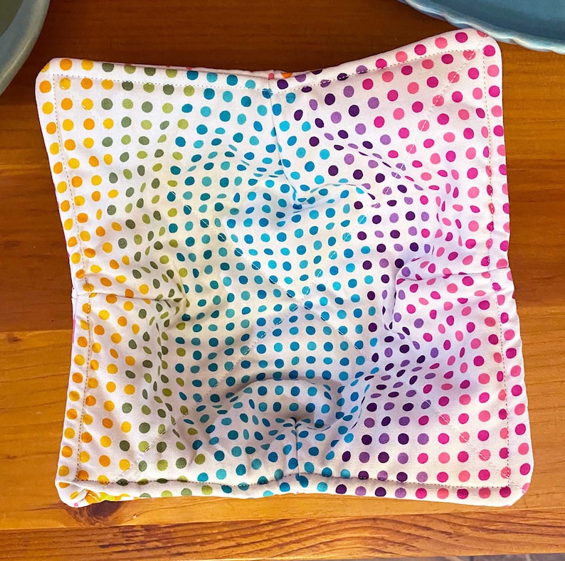May include: A colorful bowl cozy with a white background and a rainbow polka dot pattern. The cozy is made of fabric and has a quilted design.