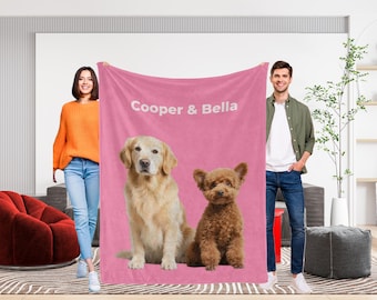 May include: A pink blanket featuring a golden retriever and a poodle, with the text "Cooper & Bella" in white. The blanket is held up by two people. The golden retriever is light brown, and the poodle is brown.