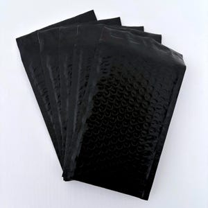 Könnte beinhalten: Fünf schwarze Luftpolstertaschen sind auf weißem Hintergrund fächerförmig angeordnet. Die Taschen haben eine glänzende, strukturierte Oberfläche mit einem Luftpolstermuster. Sie dienen zum Schutz von Artikeln beim Versand.