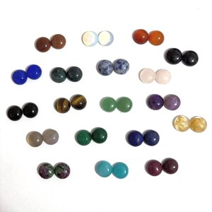 Puede incluir: Una colección de veinte pares de piedras preciosas cabujón redondas y pulidas en varios colores y texturas, incluyendo marrón, blanco, naranja, negro, azul, verde, morado, amarillo y patrones moteados, dispuestas en una cuadrícula sobre fondo blanco.