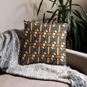 May include: A throw pillow featuring a geometric pattern in shades of brown, black, and cream. The design incorporates a repeating motif of interlocking shapes.