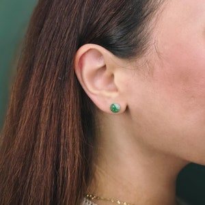 Könnte beinhalten: Eine Frau mit langen braunen Haaren trägt ein weißes Hemd und eine goldene Halskette. Sie trägt ein Paar kleine grüne und weiße Ohrringe.