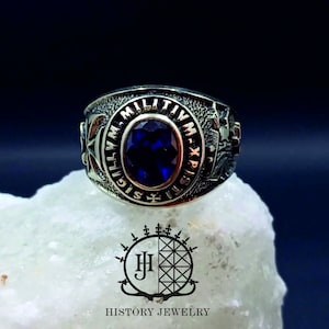 May include: A silver ring with a blue gemstone and the inscription "MILITIA M-XPI-S" around the band.