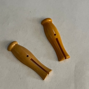 May include: Two wooden clothespins with a yellow-brown color. The clothespins have a split in the middle and a small hole on the top.