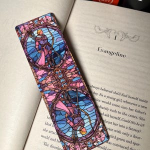 K&ouml;nnte beinhalten: Ein Lesezeichen aus Buntglas mit einem farbenfrohen Design einer Person, die einen Bogen und Pfeil h&auml;lt. Das Lesezeichen ist rechteckig und hat ein rosa, blaues und violettes Farbschema.