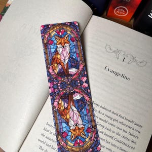K&ouml;nnte beinhalten: Ein Lesezeichen mit einem Buntglasdesign von zwei F&uuml;chsen. Die F&uuml;chse sind in einer leuchtenden Farbpalette aus Rosa, Blau und Orange dargestellt. Das Lesezeichen ist rechteckig und hat eine gl&auml;nzende Oberfl&auml;che.