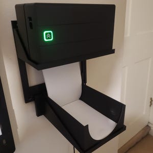May include: A black wall-mounted printer with a roll of white paper and a green light indicating it is ready to print.