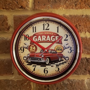 May include: A red and white wall clock with a vintage garage theme. The clock face features a classic car illustration, the words "FULL SERVICE GARAGE", and "SINCE 1956". The clock has a red metal frame and is mounted on a brick wall.