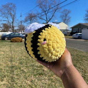 Pode incluir: Uma abelha redonda de pelúcia com listras amarelas e pretas, cabelo branco e fofo e bochechas rosadas. A abelha feita à mão é macia e aconchegante, perfeita para um brinquedo infantil ou decoração de berçário.
