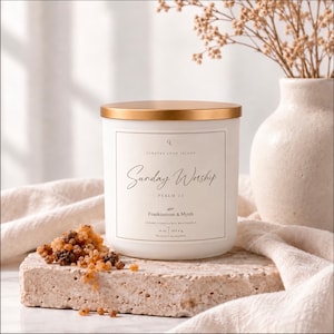 May include: A white candle in a cylindrical jar with a metallic gold lid. The label reads Curated Long Island, Sunday Worship, Psalm 23, Frankincense & Myrrh, 16 oz, 453.6 g. A pile of small, amber-colored resin pieces sits on the stone base next to it.