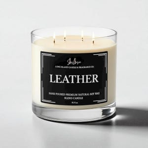 K&ouml;nnte beinhalten: Ein klares Glas-Kerzenglas mit vier Dochten, gef&uuml;llt mit cremefarbenem Wachs. Ein schwarzes Etikett mit wei&szlig;em Text lautet "LEATHER" und "HAND POURED PREMIUM NATURAL SOY WAX BLEND CANDLE". Die Kerze wiegt 1013 Gramm.
