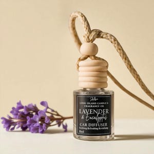 May include: A car air freshener with a wooden top and a clear glass bottle. The label reads "Lavender & Eucalyptus" and "Car Diffuser". A sprig of purple flowers and a beige rope are also in the image.