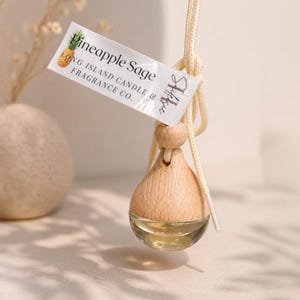 May include: A hanging car air freshener with a wooden top and a clear glass bottom filled with liquid. A tag reads "Pineapple Sage" and "Long Island Candle & Fragrance Co."
