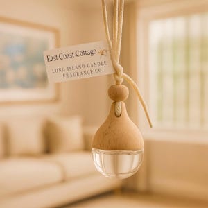 May include: A hanging air freshener with a wooden top and a clear glass bottom. The air freshener is suspended by a cream-colored string and has a tag that reads "East Coast Cottage, Long Island Candle Fragrance Co."