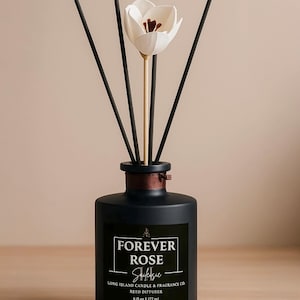 May include: Black glass reed diffuser bottle with black sticks and a white flower. The label reads "FOREVER ROSE Saiksie LONG ISLAND CANDLE & FRAGRANCE CO. REED DIFFUSER 6 fl oz | 177 ml"
