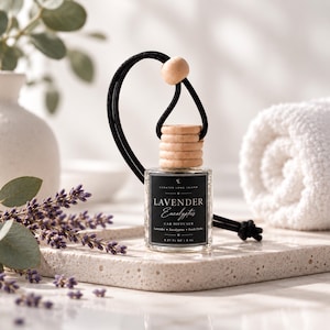 May include: A small clear glass car diffuser bottle with a black label reading Lavender Eucalyptus Car Diffuser 0.27 FL OZ | 8 ML. The bottle features a ribbed wooden cap and a black cord with a wooden bead for hanging, designed for scent diffusion.