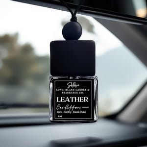 May include: Black car air freshener with a black and white label that reads "Safelsie Long Island Candle & Fragrance Co. Leather Car Diffuser - Rich, Earthy, Musk, Bold 8ml"