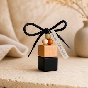 May include: A decorative air freshener with a black shoelace bow, wooden beads, and two stacked cubes. The top cube is natural wood, the bottom is black. A tag reads "Sandalwood & Bergamot".