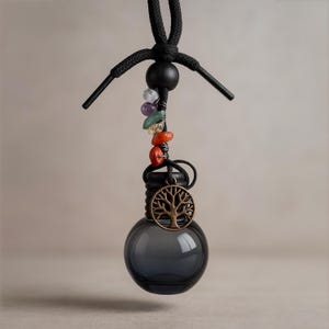 May include: A dark gray glass aromatherapy diffuser with a black cord and a decorative tree of life charm. The diffuser is adorned with colorful gemstones and is designed to hang. The overall design is intended for aromatherapy.