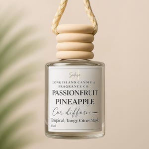 May include: A clear glass bottle with a white label that reads "Passionfruit Pineapple Car Diffuser - Tropical, Tangy, Citrus, Musk" and "Long Island Candle & Fragrance Co." The bottle has a wooden cap and a beige rope hanger.