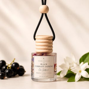 May include: A glass car diffuser bottle with a light wood cap and black hanging cord. The label reads: Curated Long Island, Black Currant Jasmine, Car Diffuser, Romantic, Citrusy, Floral, 0.27 fl oz | 8 ml. Dried flowers are visible inside.