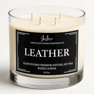 K&ouml;nnte beinhalten: Eine klare Glaskerze mit cremefarbenem Wachs und drei Dochten. Das schwarze Etikett tr&auml;gt die Aufschrift "LEATHER" und "35.75 oz". Die Kerze stammt von Long Island Candle & Fragrance Co.