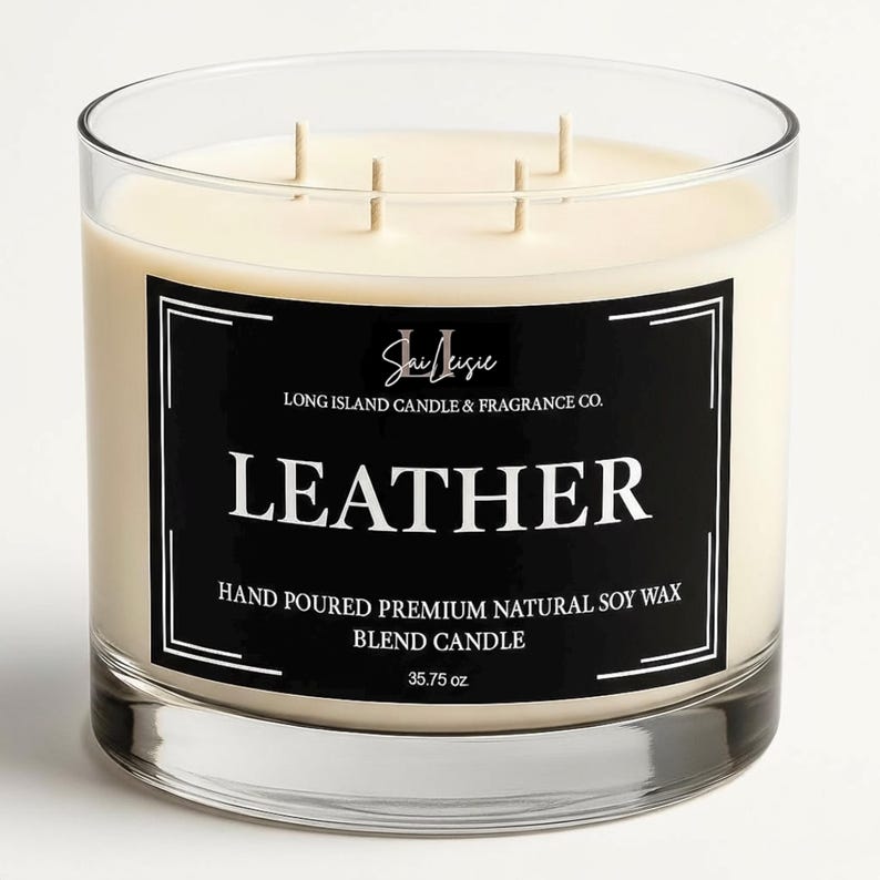 K&ouml;nnte beinhalten: Eine klare Glaskerze mit cremefarbenem Wachs und drei Dochten. Das schwarze Etikett tr&auml;gt die Aufschrift "LEATHER" und "35.75 oz". Die Kerze stammt von Long Island Candle & Fragrance Co.