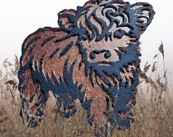 May include: A decorative Highland cow figurine with a textured, layered design. The cow features a brown body with dark blue accents, standing in a field of tall grass. The figurine has a unique, artistic appearance.