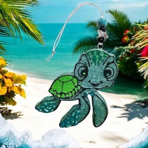 May include: A green and blue sea turtle charm with glitter accents. The turtle is hanging from a white string with a silver starfish and black beads.